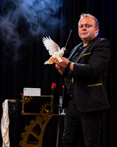 Odeeni Circus of Illusion magician performing dove magic with a white dove on stage.