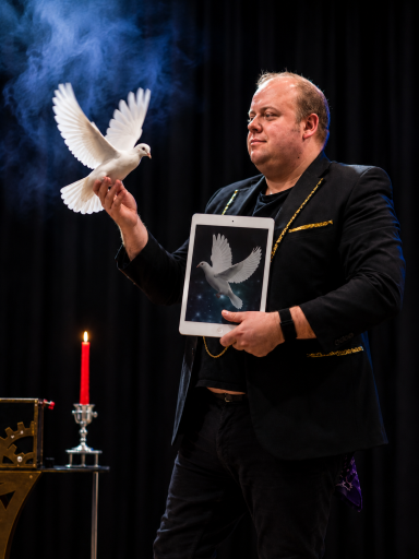 Odeeni Circus of Illusion magician performing with a white dove during a live stage magic show.