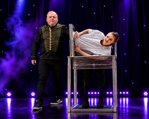 Odeeni Circus of Illusion magician and assistant performing a dramatic stage illusion under purple theatrical lighting.